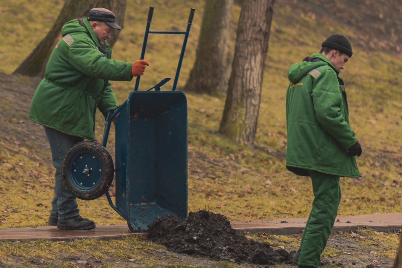 Three Greenfold landscapers in work clothes, smiling in a garden with wheelbarrows, tools and paving materials around them.